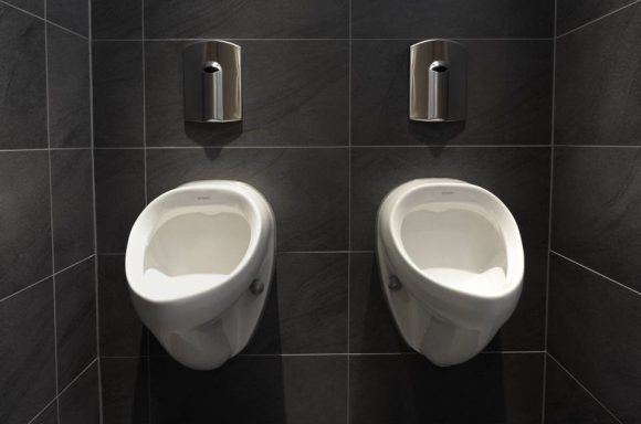 Zwei weiße Urinale an einer dunklen Wand in einem Männerbadezimmer.