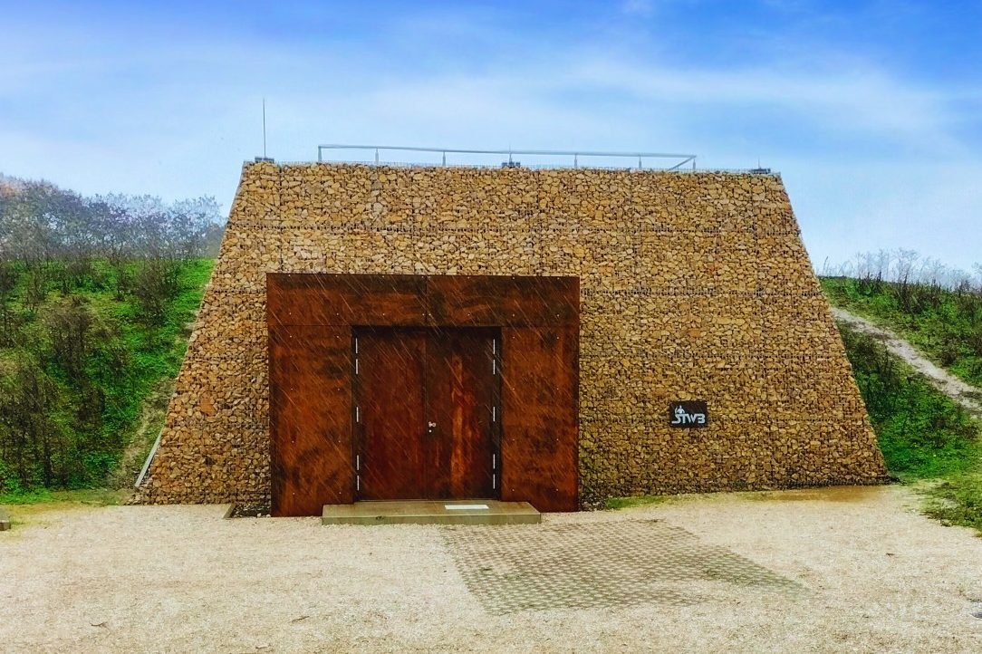 Publikation Hochbehälter Rothof Eingang zu einem steinernen Gebäude mit einem Holztor, umgeben von grüner Landschaft.