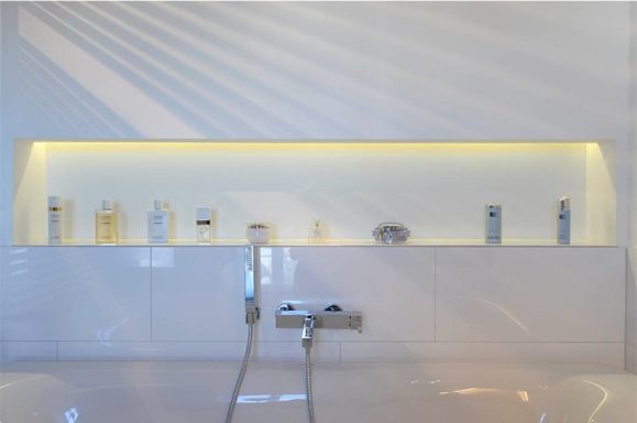 Moderne Badewanne mit beleuchtetem Regal und verschiedenen Pflegeprodukten.